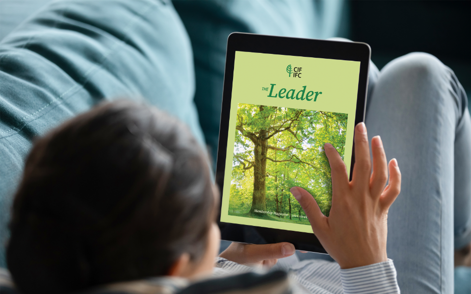 The-Leader-3 Woman laying on a couch reading the membership magazine on a tablet.