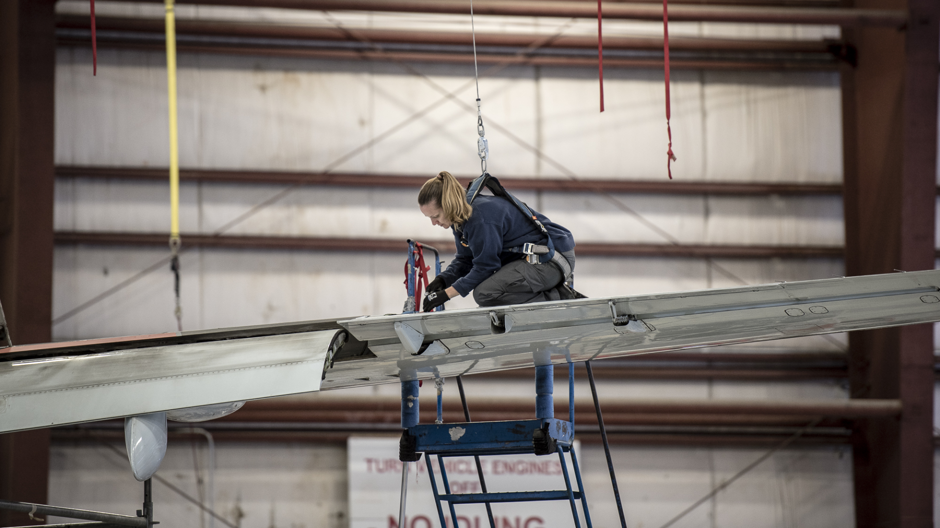 Chorus-Aviation-Frame-11 Female airplane mechanic kneeling on wing of plane making repairs.