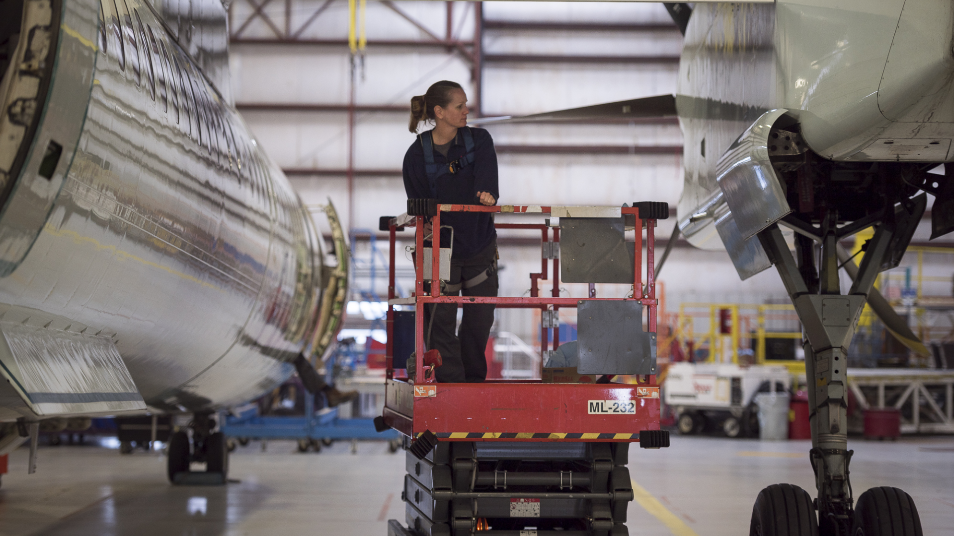 Chorus-Aviation-Frame-12 Female airplane mechanic on a scissor-lift inspecting the landing gear of an airplane.