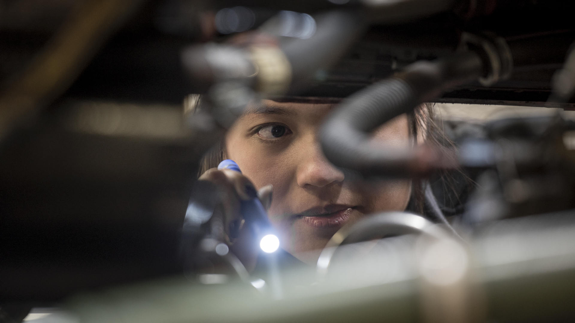 Chorus-Aviation-Frame-8 Young female airplane mechanic looking inside an engine with a flashlight.