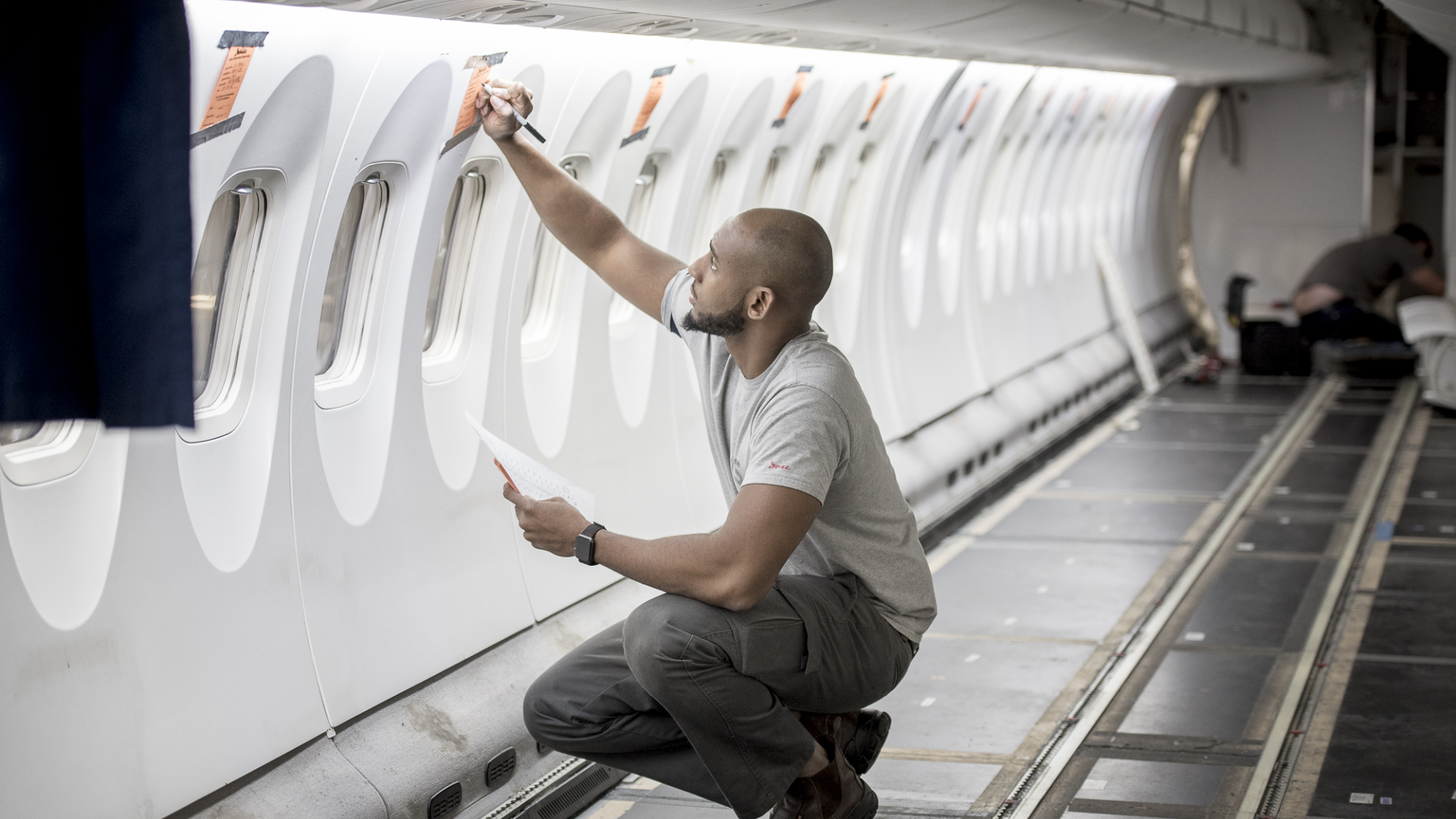 Chorus-Aviation-Frame-9 Young male employee kneeling inside an airplane without any passenger seats.