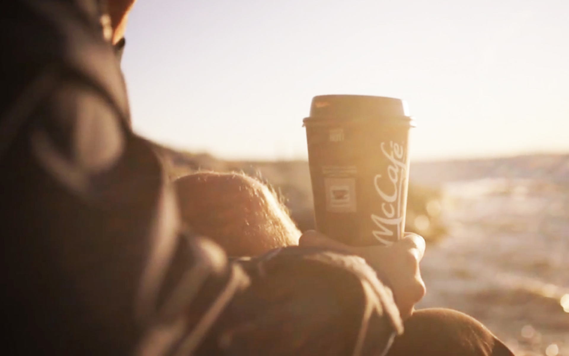 Young man holding a McCafe premium roast coffee specialty drink while enjoying the sunset .