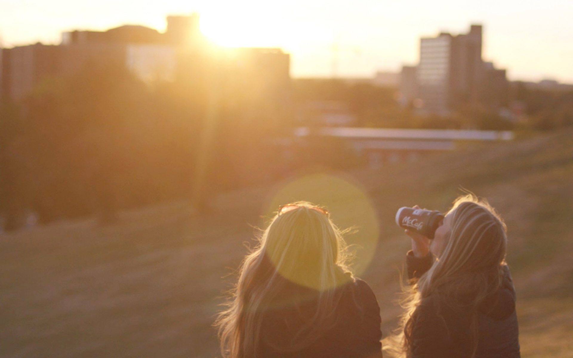 Two young women enjoying a McCafe premium roast specialty coffee while enjoying the sunset at Citadel Hill in Halifax.