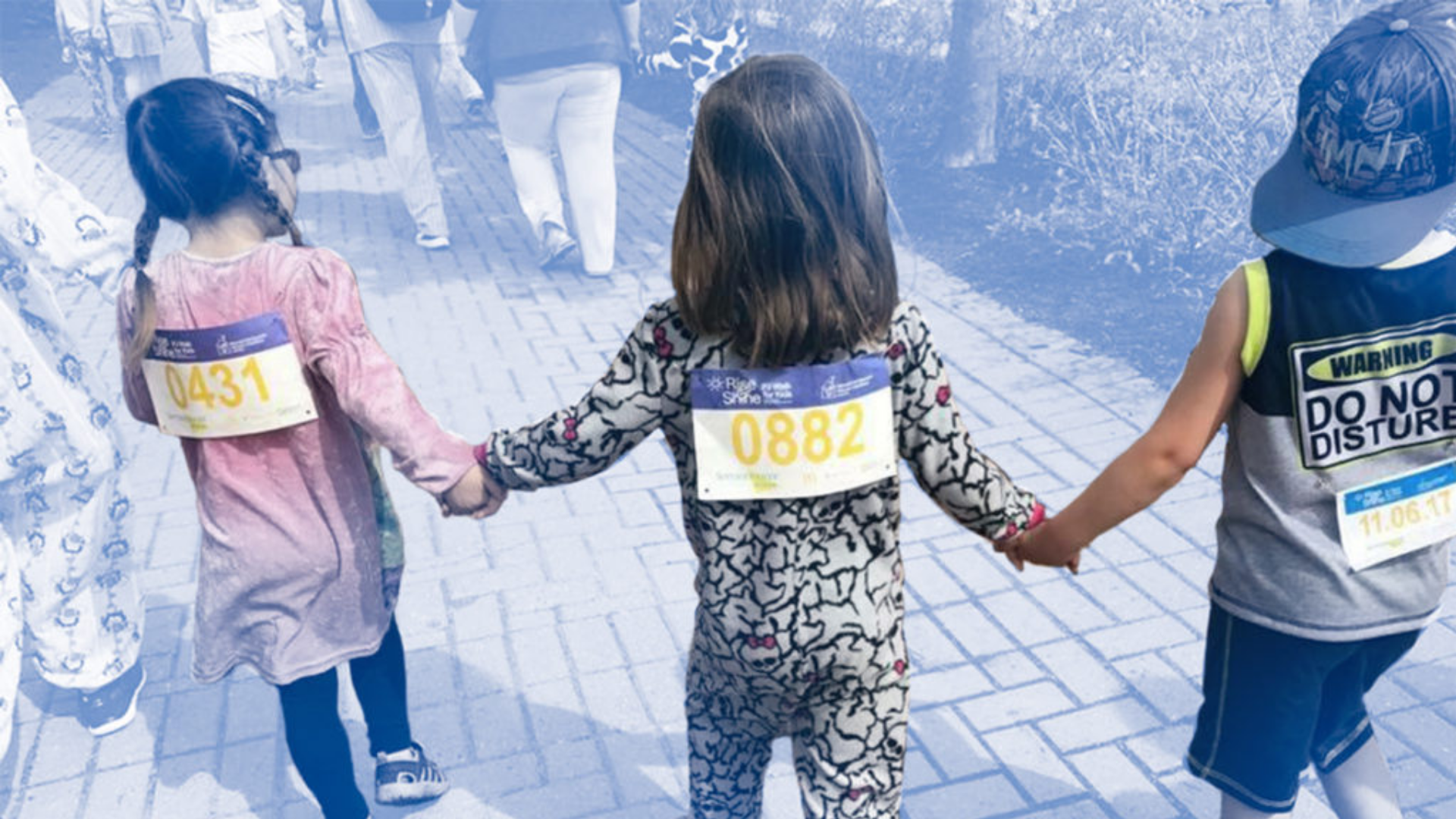 RMHCA-PJ-Walk-for-Kids-2 Three young girls hold hands while wearing pyjamas and racing bibs.